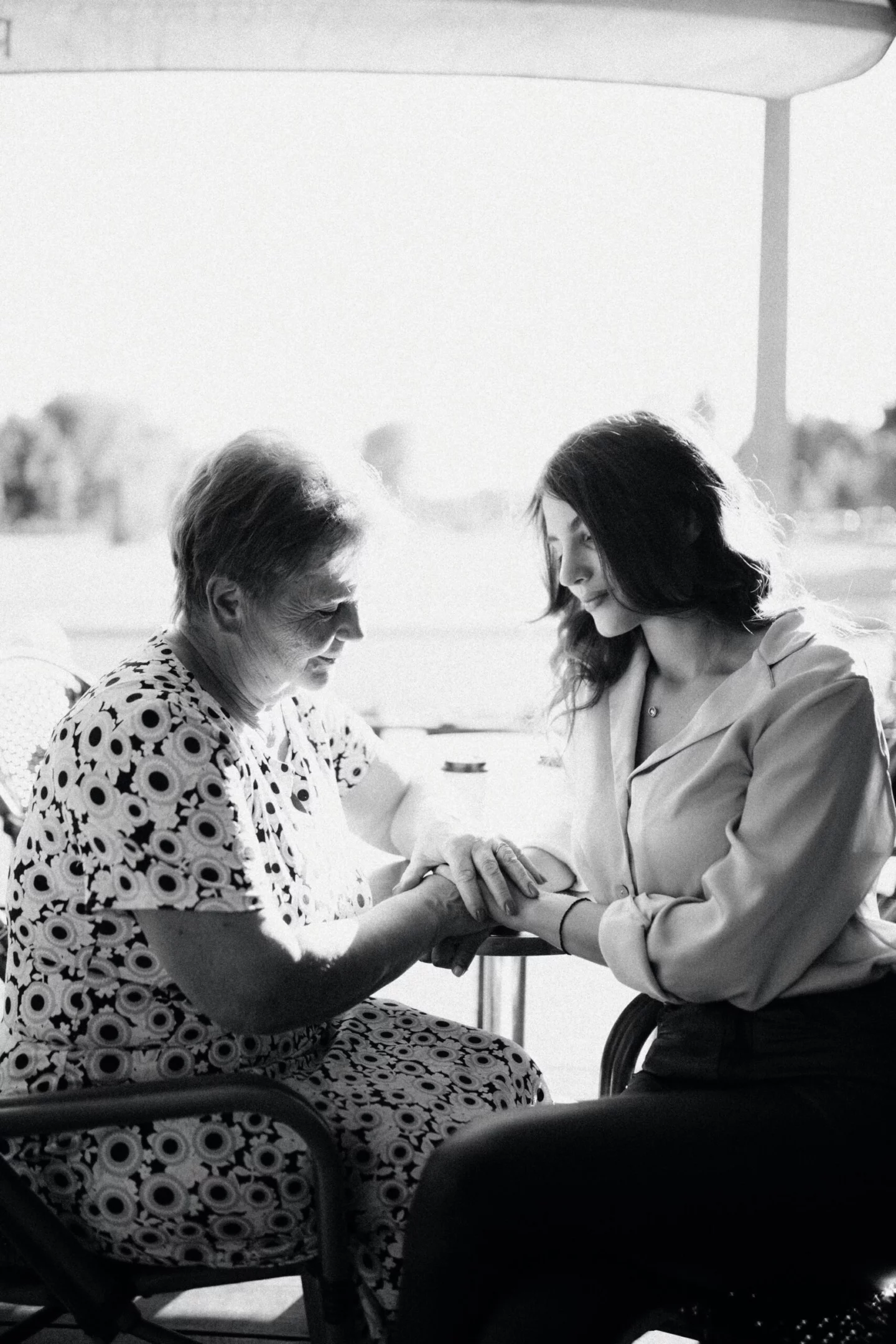 Younger woman hand-in-hand with older woman comforting here by a large window