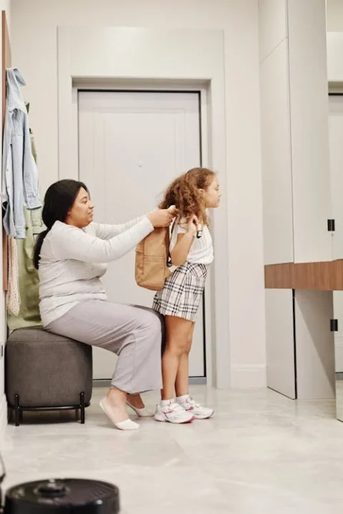Mother helping young child put her backpack on before leaving for school